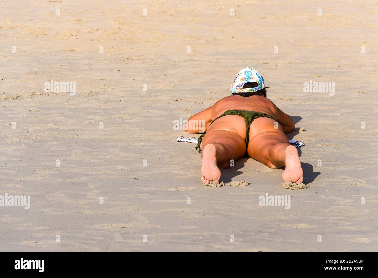Eine übergewichtige Frau liegt beim Sonnenbaden am Strand auf dem Bauch Stockfoto