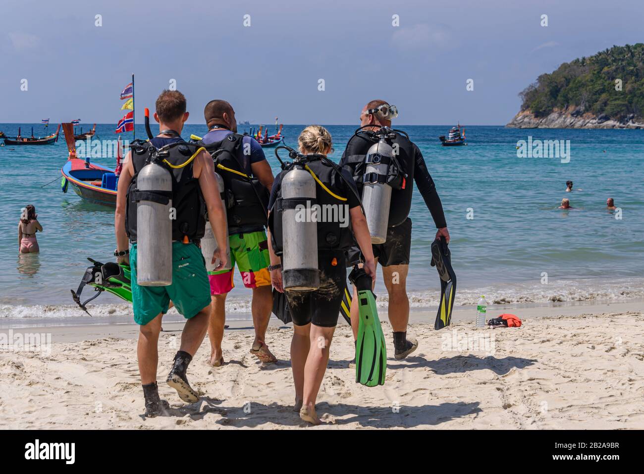 Vier Taucher mit Sporttanks gehen in Richtung Meer am Kata Beach, Phuket, Thailand Stockfoto