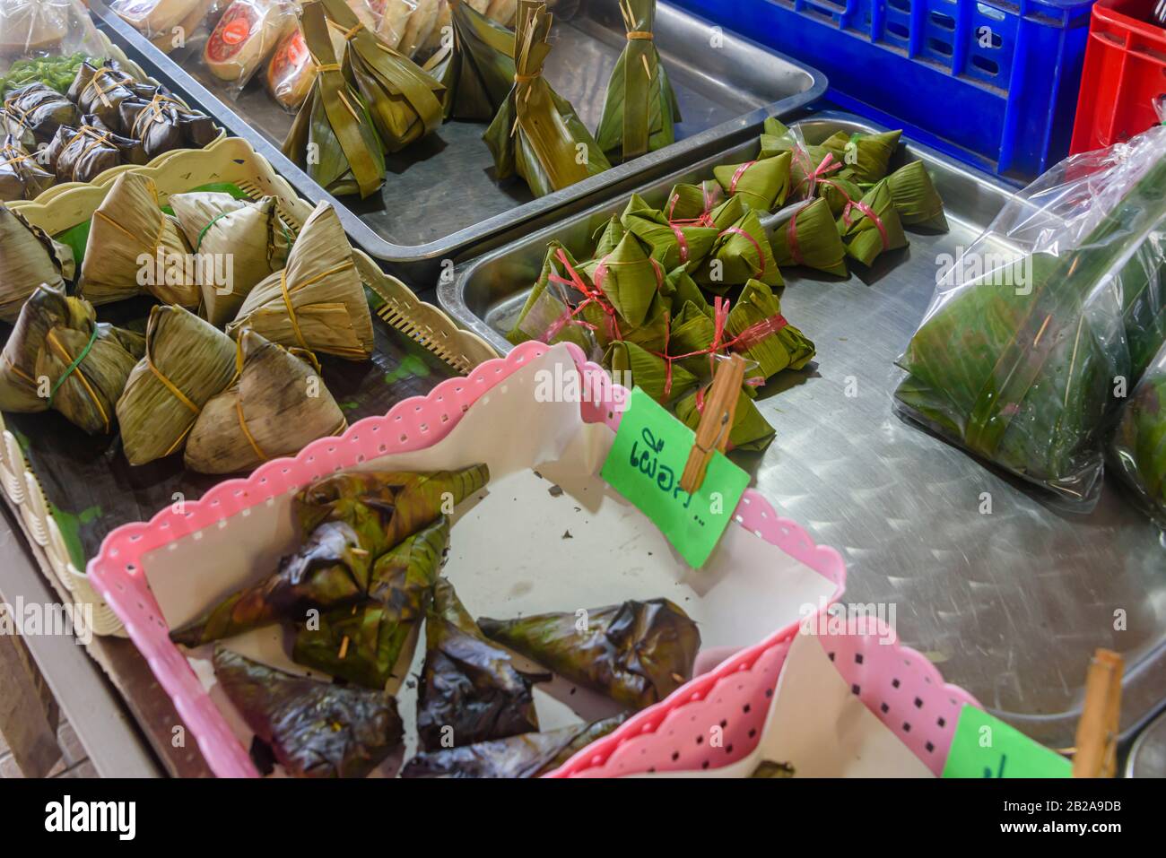 Klebrige Reiskugeln, die mit Bananenblättern umhüllt sind, die in einem thailändischen Marktstall in Thailand zum Verkauf angeboten werden Stockfoto