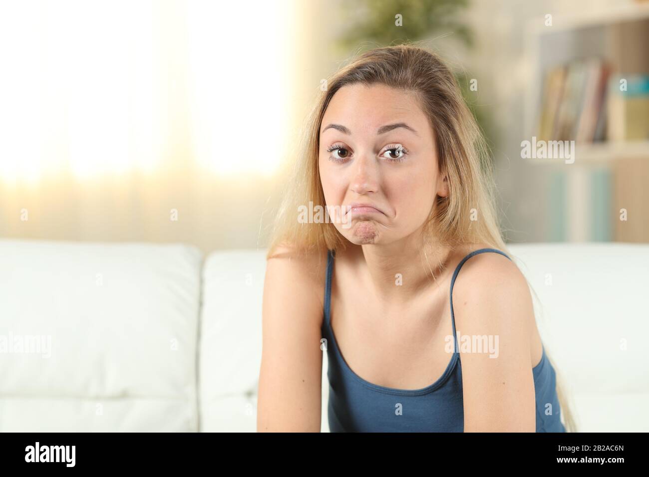 Zögerliches Mädchen im Teenager-Alter, das auf einer Couch im Wohnzimmer die Kamera betrachtet Stockfoto