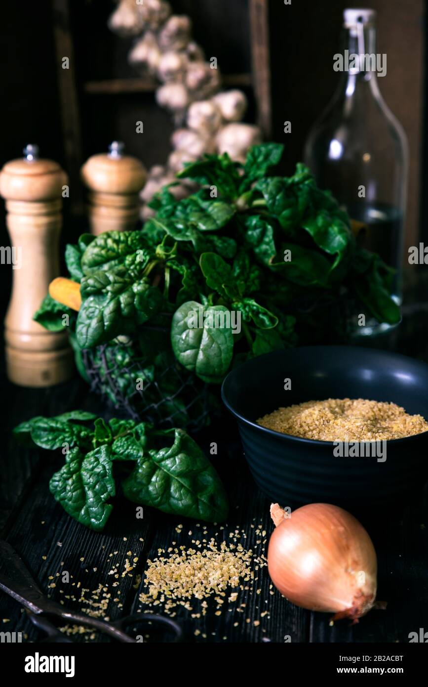 Spinat, Zwiebel, Knoblauch und Bulgur auf einem Holztisch Stockfoto