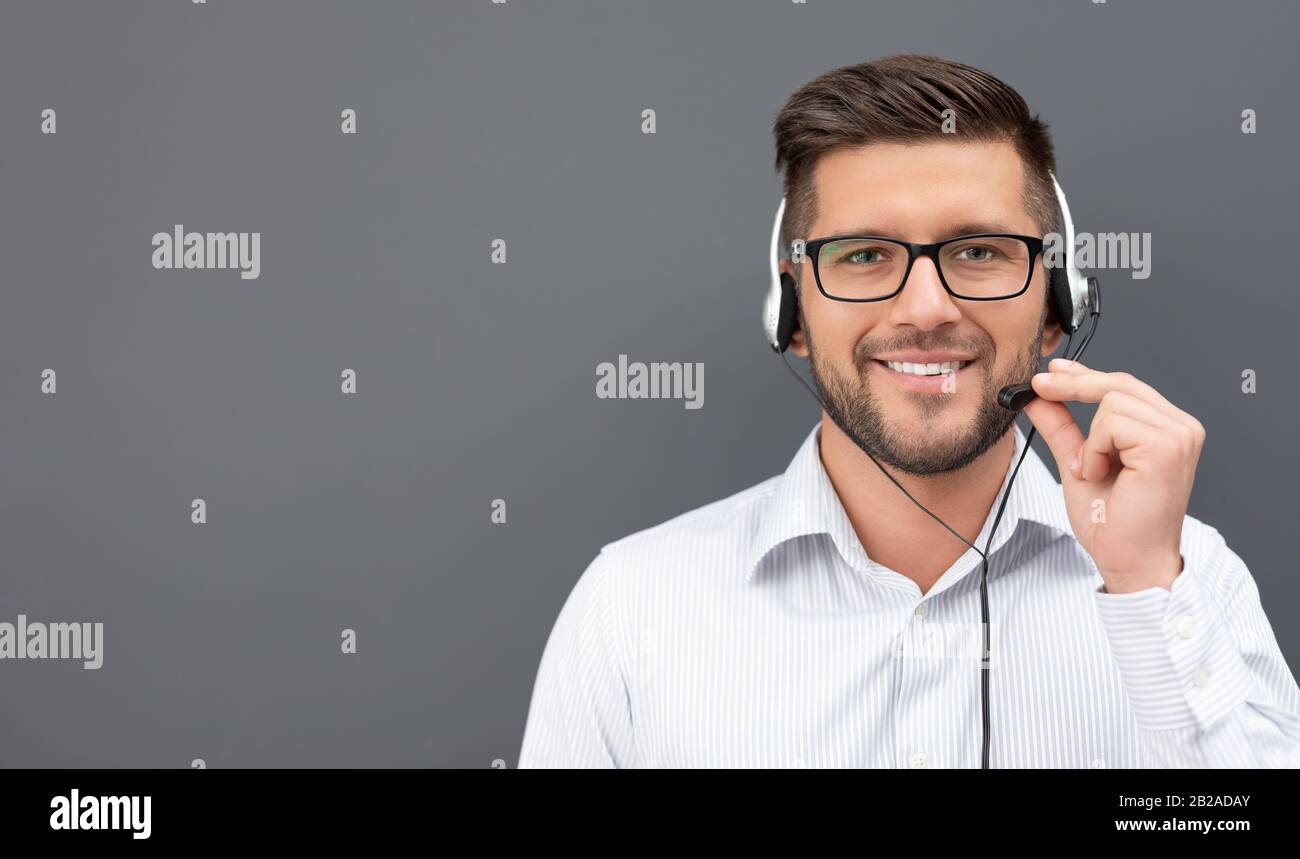 Call Center-Mitarbeiter isoliert auf grauem Hintergrund. Lächelnder Kundendienstanbieter bei der Arbeit. Junge Mitarbeiter, die mit einem Headset arbeiten. Stockfoto