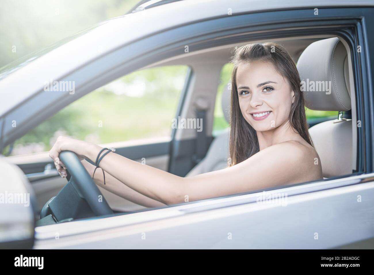 Schöne junge Frau, die mit einem Lächeln im Innenraum eines neuen Autos sitzt. Er ist froh, dass er ein Fahrer ist. Stockfoto