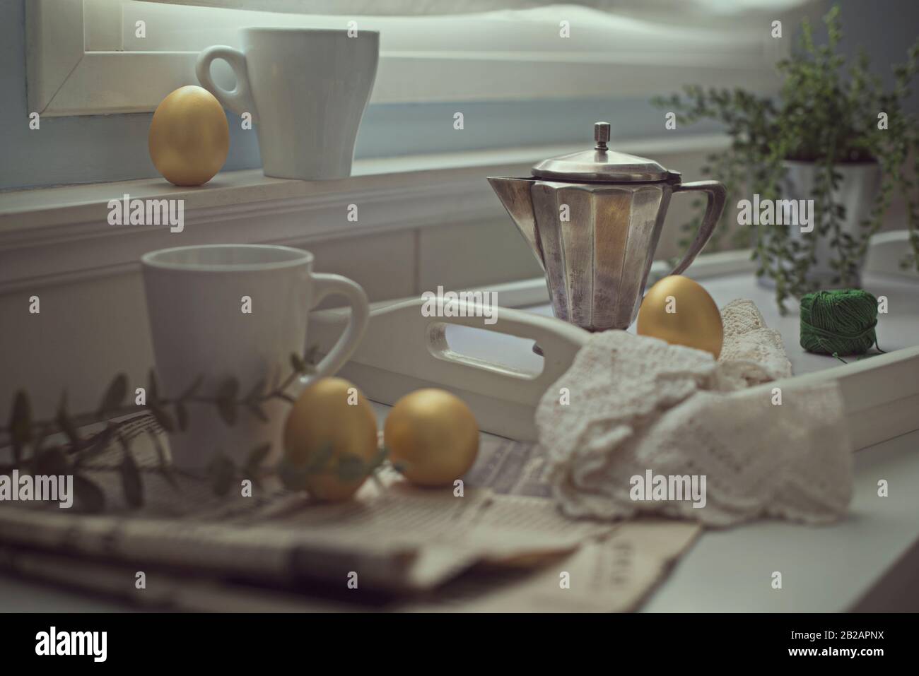 Goldene Ostereier auf einer Küchenecke mit Tassen, Zeitung und Kaffeekanne Stockfoto