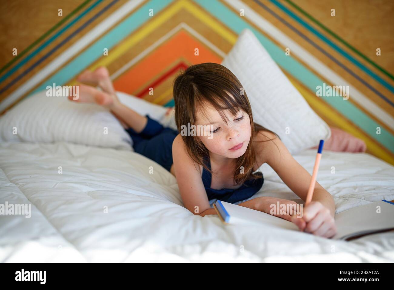 Portrait eines Mädchens, das auf ihrem Bett liegt und seine Hausaufgaben macht Stockfoto