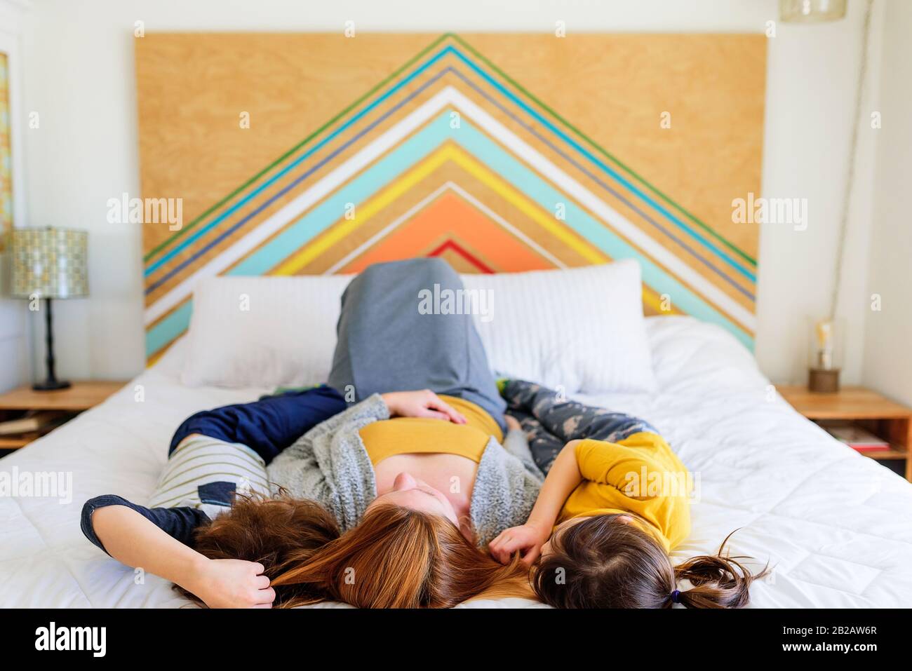 Mutter liegt mit ihren beiden Kindern, die mit ihren Haaren spielen, im Bett Stockfoto