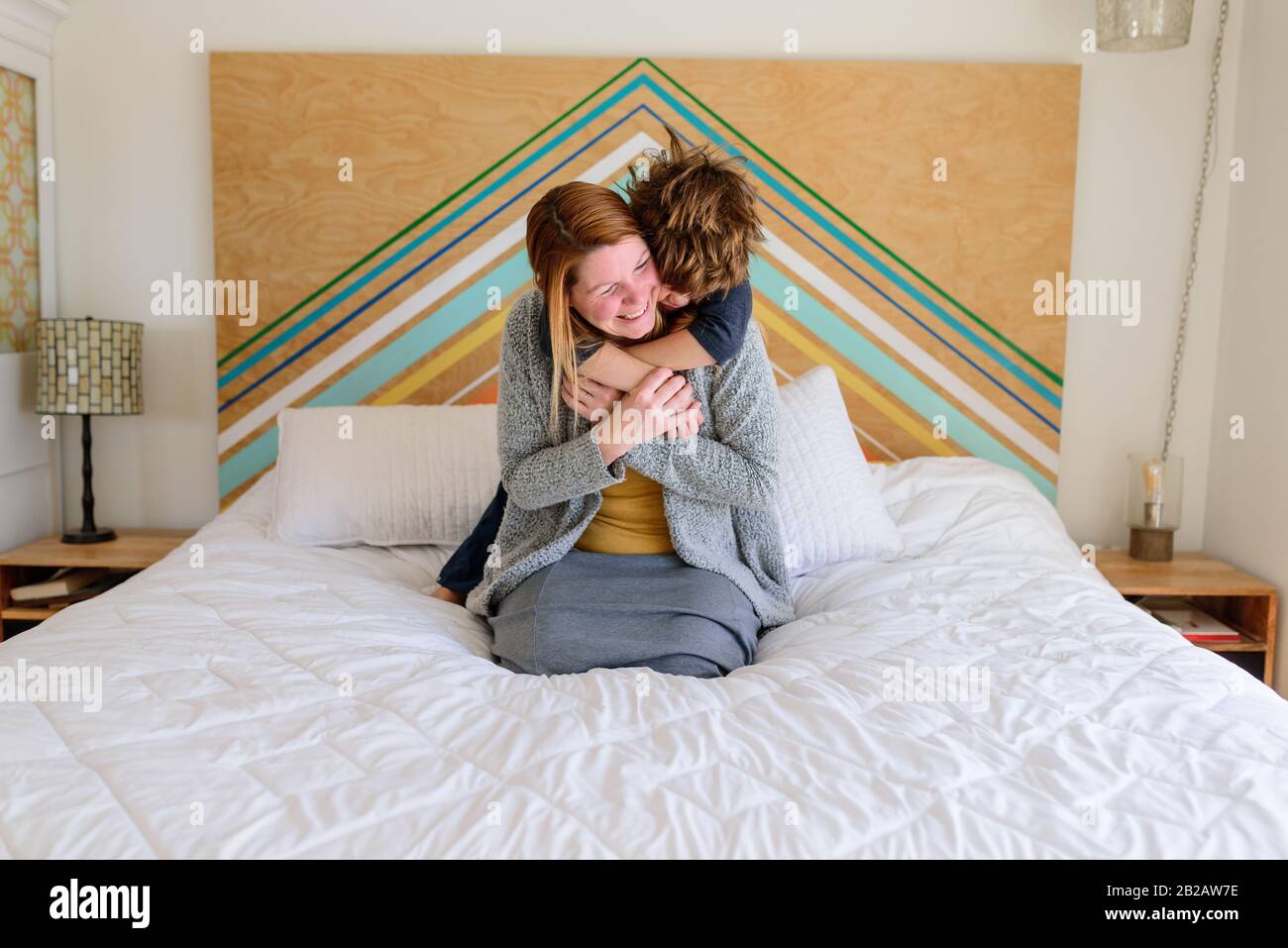 Junge, der auf einem Bett steht und seine Mutter kuschelt Stockfoto