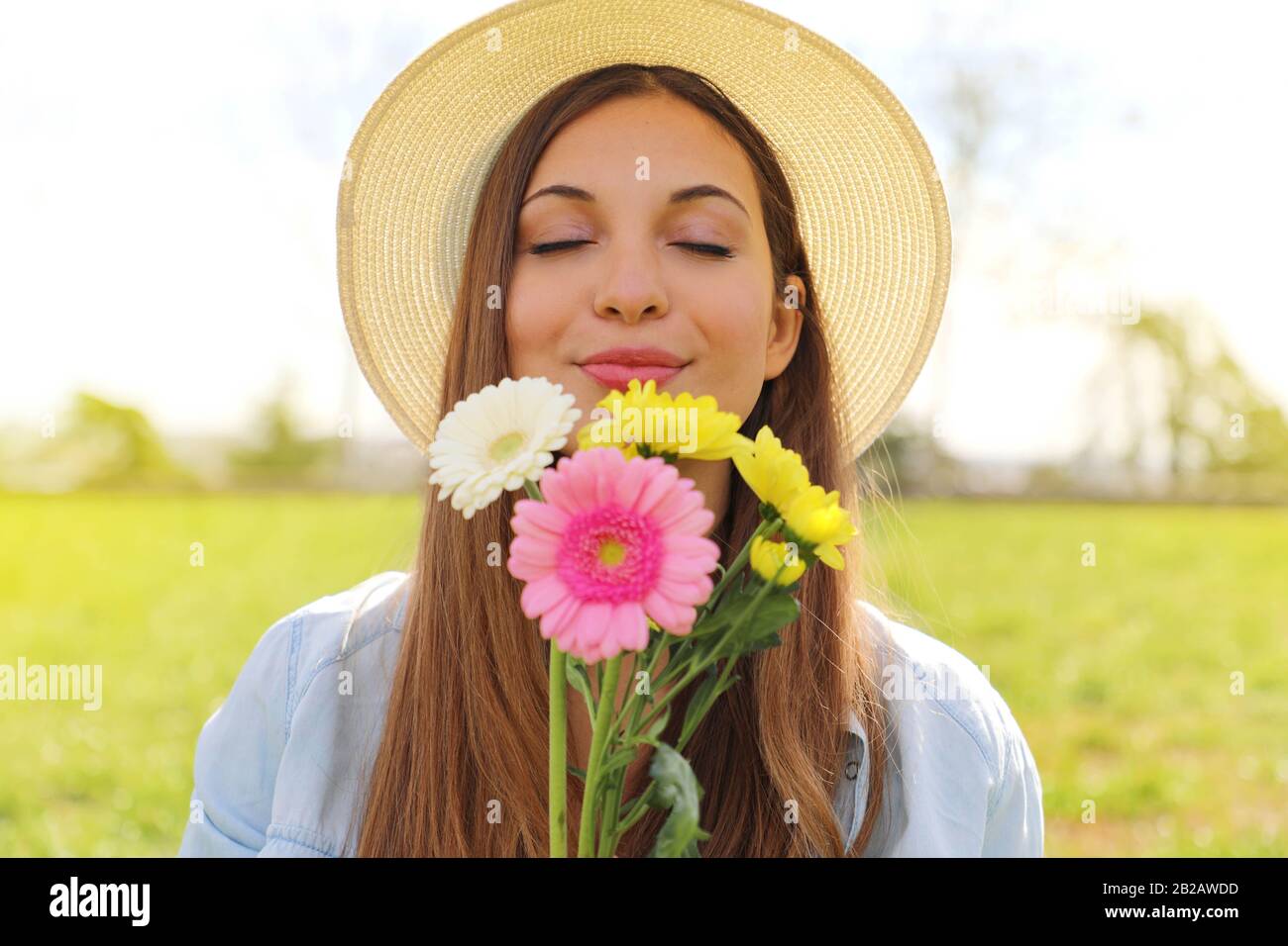 Schönes junges Mädchen mit geschlossenen Augen und Hut riechender Blumenstrauß im Frühjahr Stockfoto