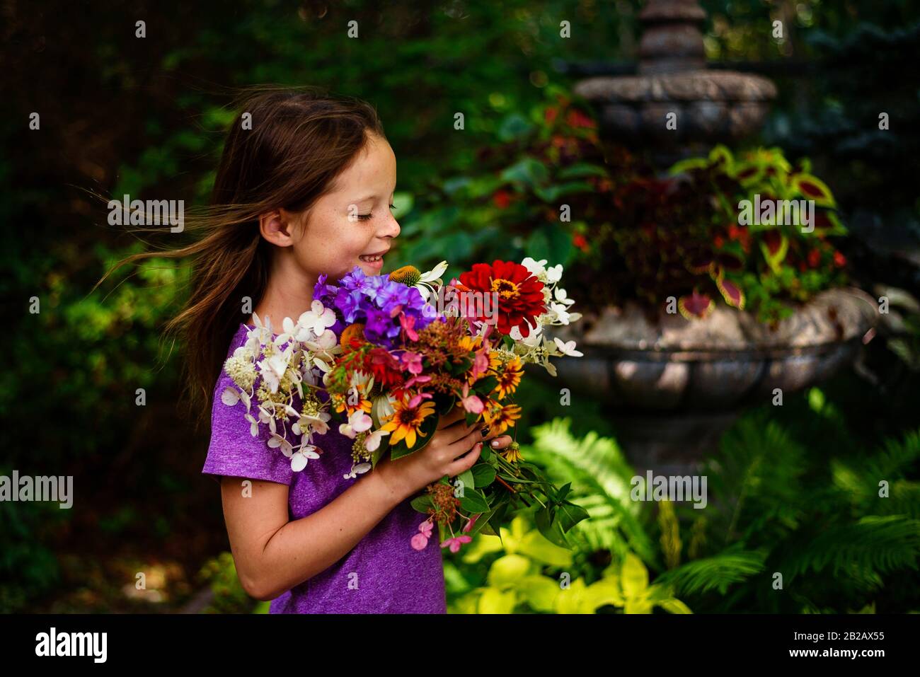 Porträt eines lächelnden Mädchens, das in einem Garten steht, der einen Haufen Blumen hält, USA Stockfoto