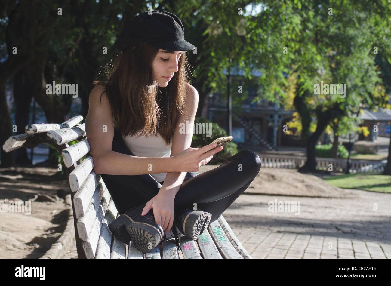 Teenager-Mädchen, die auf einer Parkbank sitzen und ihr Telefon, Argentinien, überprüfen Stockfoto