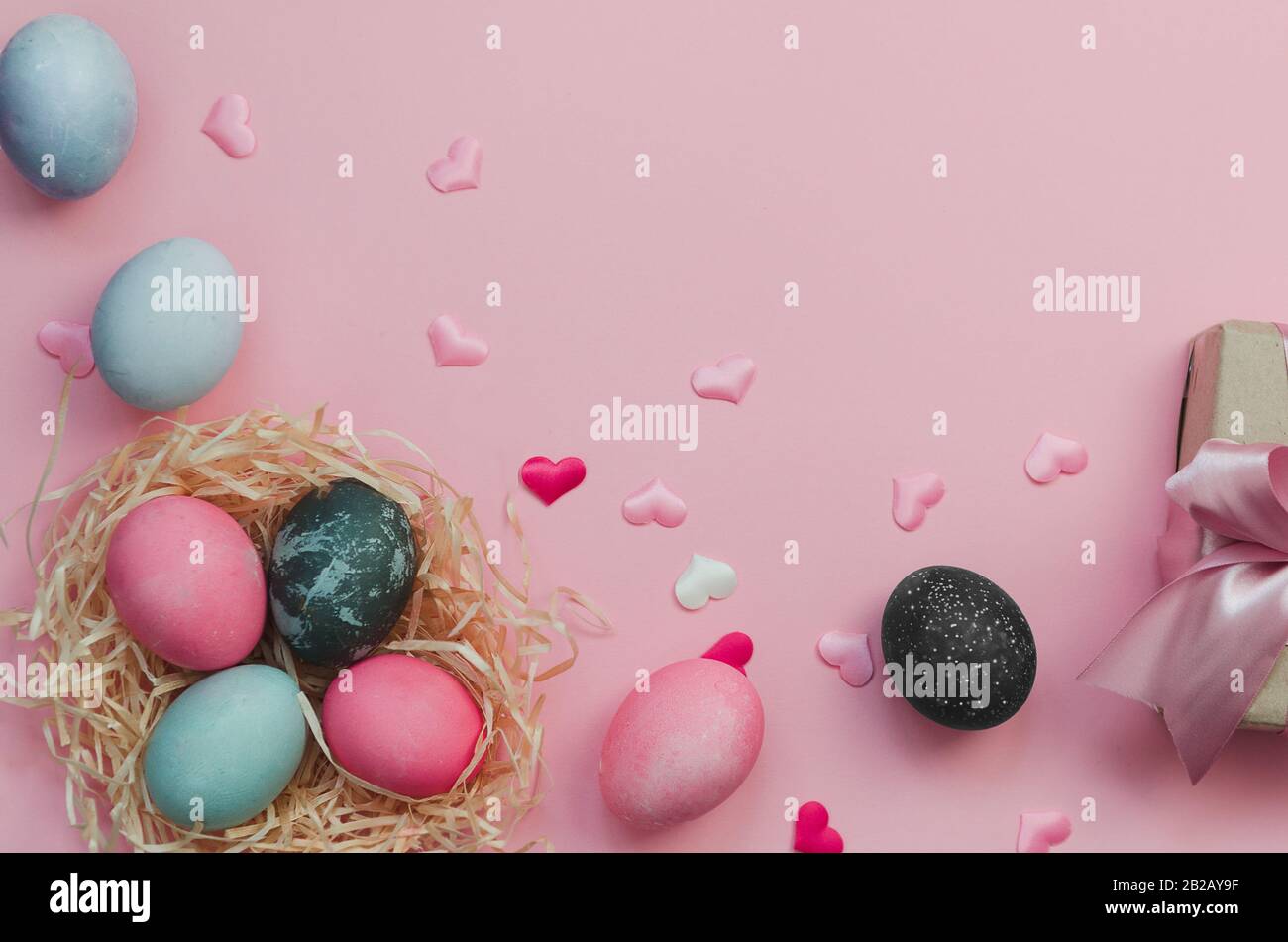 Ostereier und Nestlé mit bunten Eiern und Herzen auf rosa Hintergrund Stockfoto