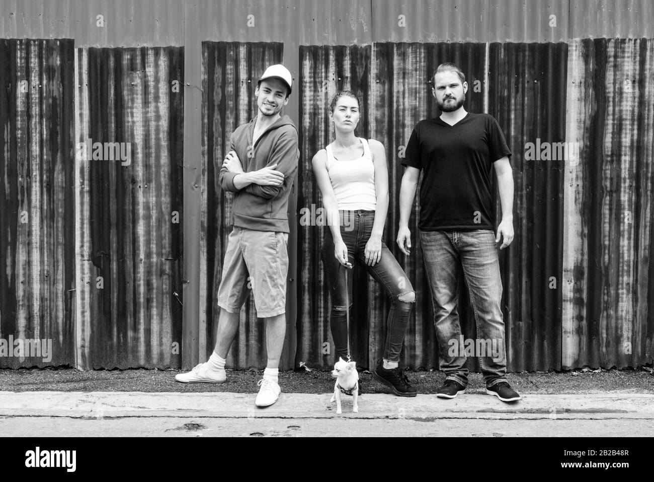 Happy Gruppe von Freunden Lächeln und während Gegen alten rostigen Blech Wand mit Frau mit niedlichen Hund posing Stockfoto