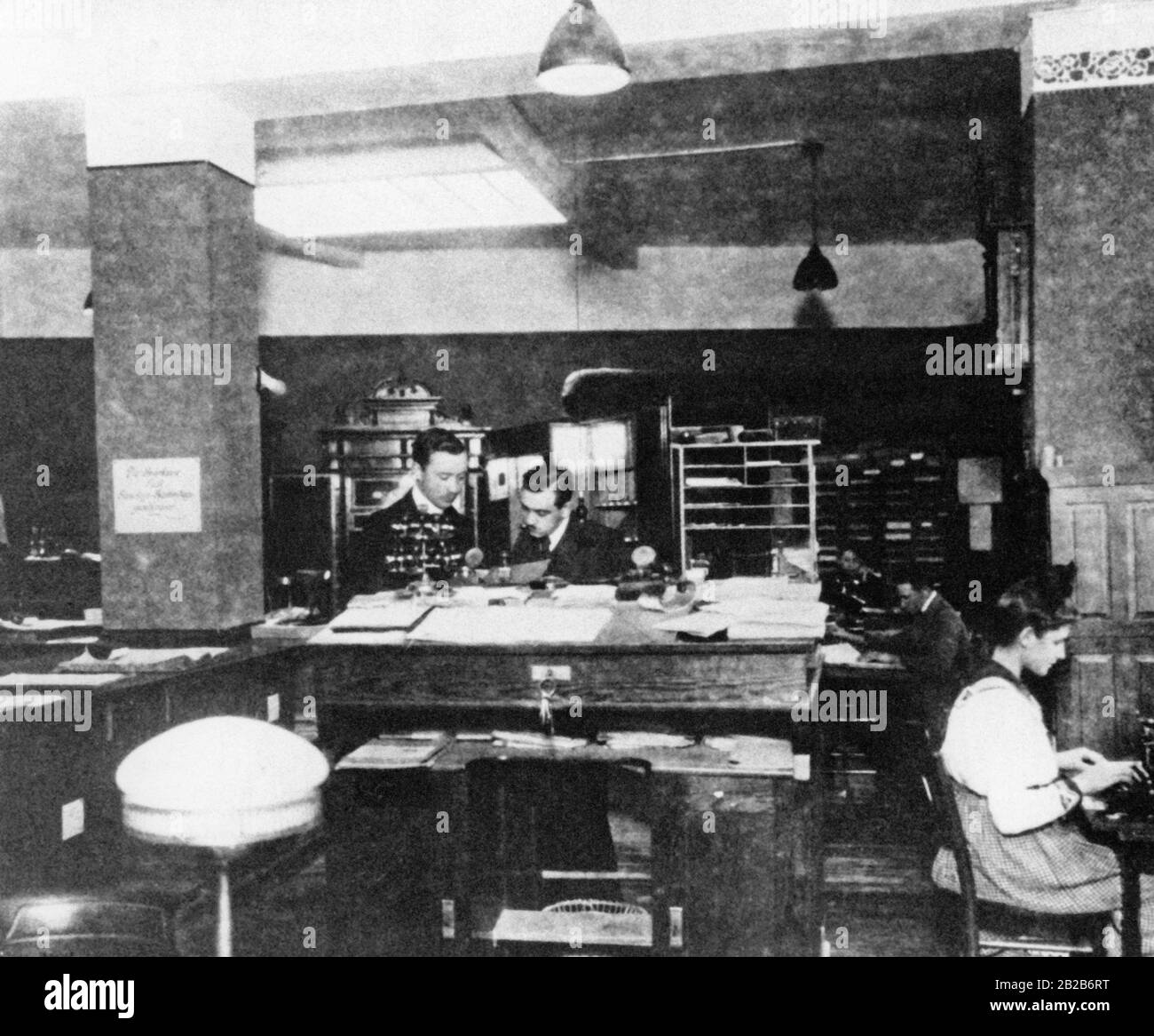 Das Foto zeigt Mitarbeiter in einem typischen Büroumfeld um die Jahrhundertwende. Auf der rechten Seite des Bildes befindet sich eine Sekretärin, die an einer Schreibmaschine arbeitet, was im frühen 20. Jahrhundert eine recht verbreitete Szene war. Stockfoto