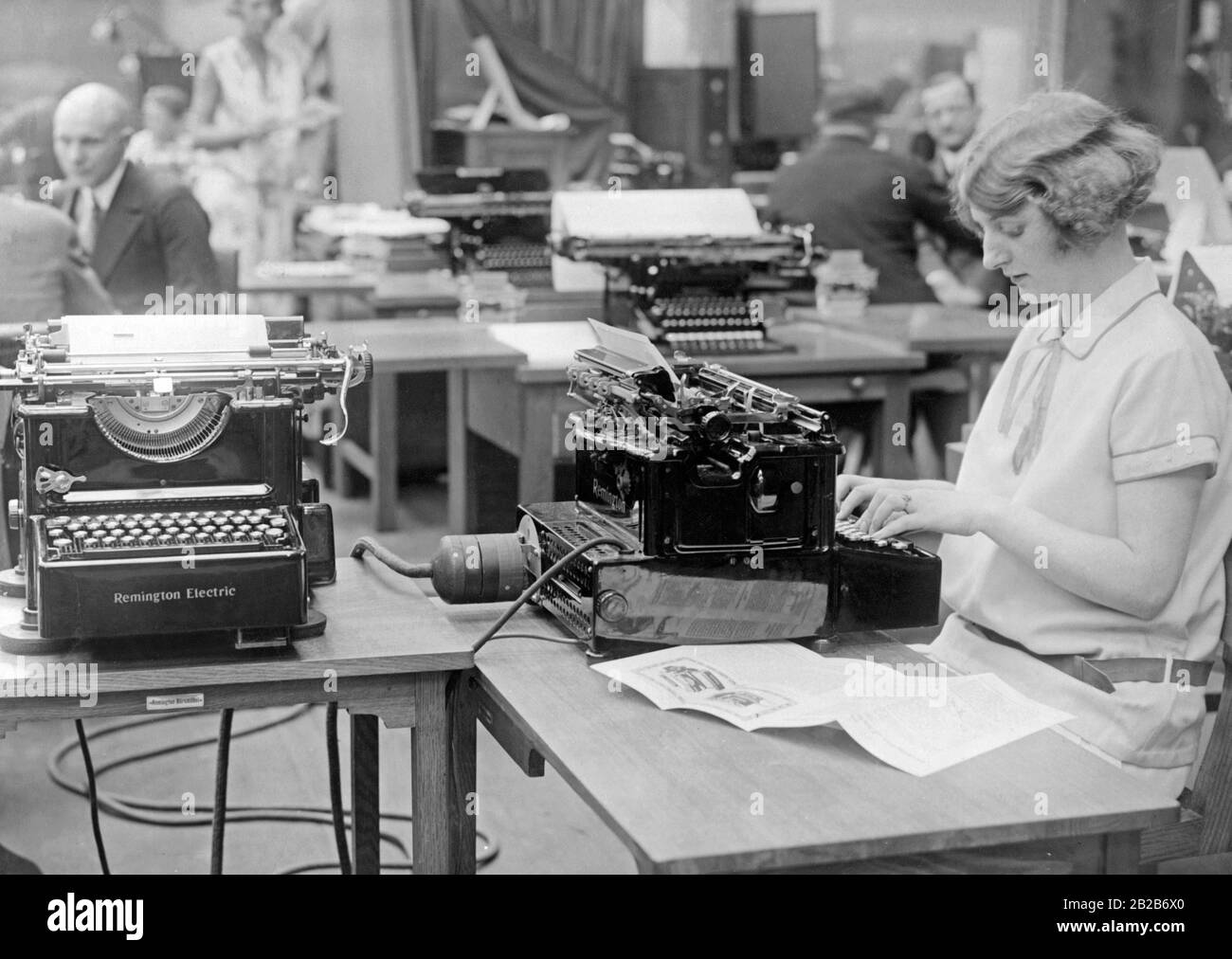 Eine Frau betreibt sechs Schreibmaschinen gleichzeitig. Das Bild wurde anlässlich der Eröffnung der Internationalen Büroausstellung am Kaiserdamm in Berlin veröffentlicht. Es präsentiert die neue Remington Electric, eine Neuerung der Remington Society, die den gleichzeitigen Einsatz mehrerer Maschinen mittels elektrischer Kupplung ermöglichte. Stockfoto