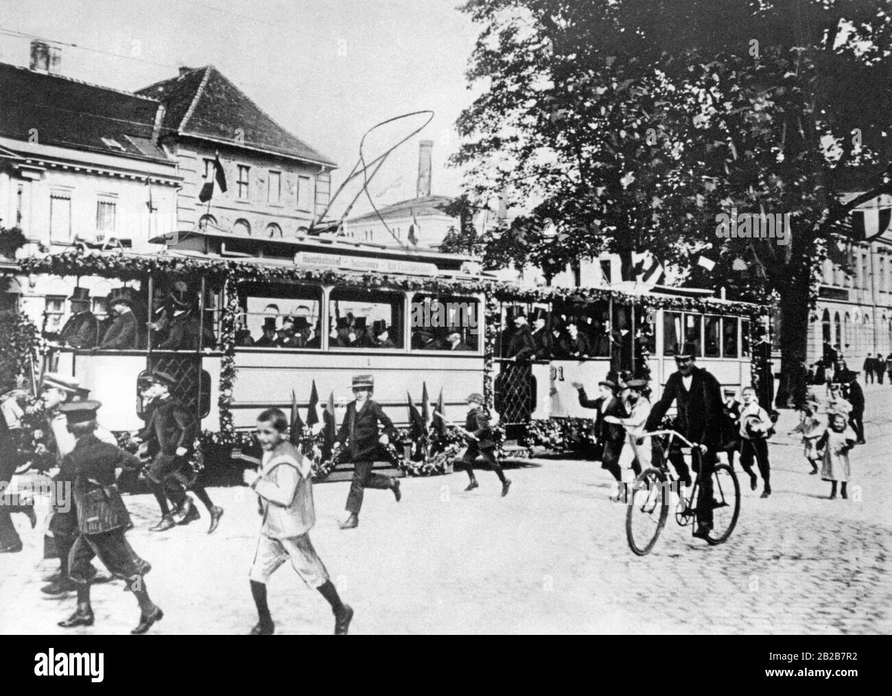 September 1907 die erste elektrische Straßenbahn in Potsdam bei ihrer feierlichen Eröffnung. Zwischen Hauptbahnhof, Sanssouci und Bahnhof Charlottenburg verlief die Strecke mit Förderwagen der Firma "Gottfried Lindner AG". Kinder gehen neben der Straßenbahn, die mit Blumen und Fahnen dekoriert ist. Stockfoto