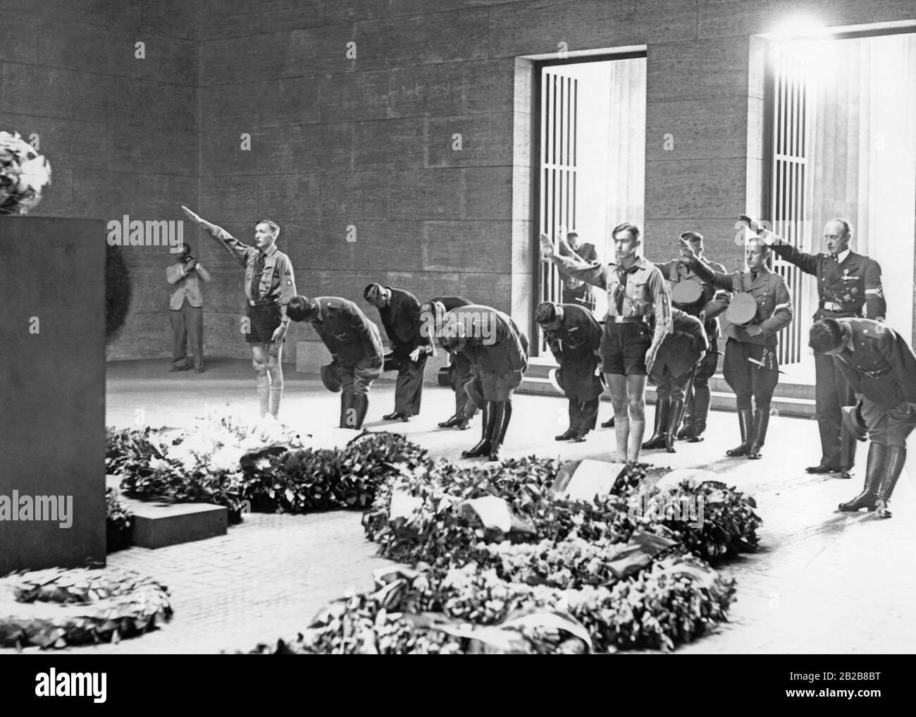Die Führung einer japanischen Jugendorganisation beugt sich nach der Kranzniederlegung vor der Gedenkstätte unter den Linden in Berlin. Begleitet werden sie von Angehörigen der Reichs-Jugend-Führung, die den Nazi-Salut vollbringen. Stockfoto