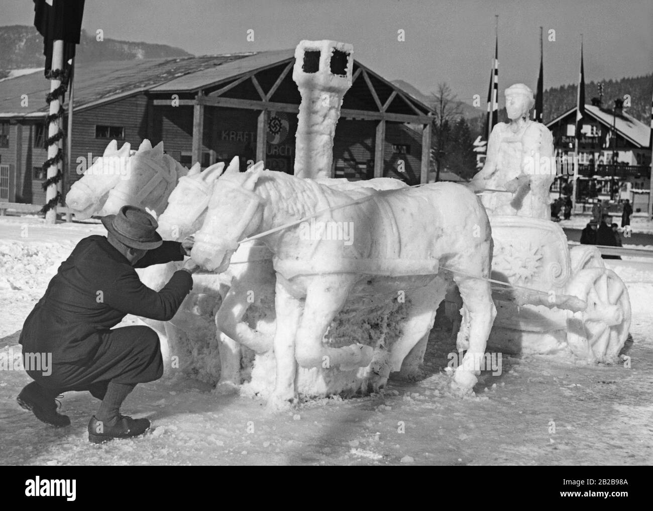 Anlässlich der Olympischen Winterspiele in Garmisch-Partenkirchen schuf ein Künstler eine Schneeskulptur "Roman Quadriga". Im Hintergrund stand die K.D.F. Festhalle. Stockfoto