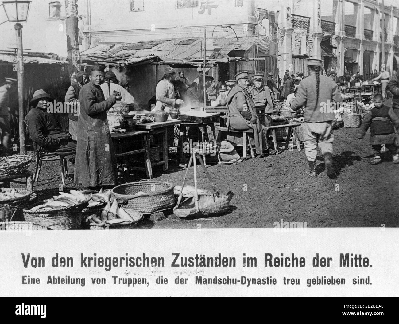 Blick entlang einer Straße in China während der chinesischen Revolution. An einigen Tischen sitzen und essen kaiserliche Truppen. Viele Menschen gehen auf die Straße. Stockfoto