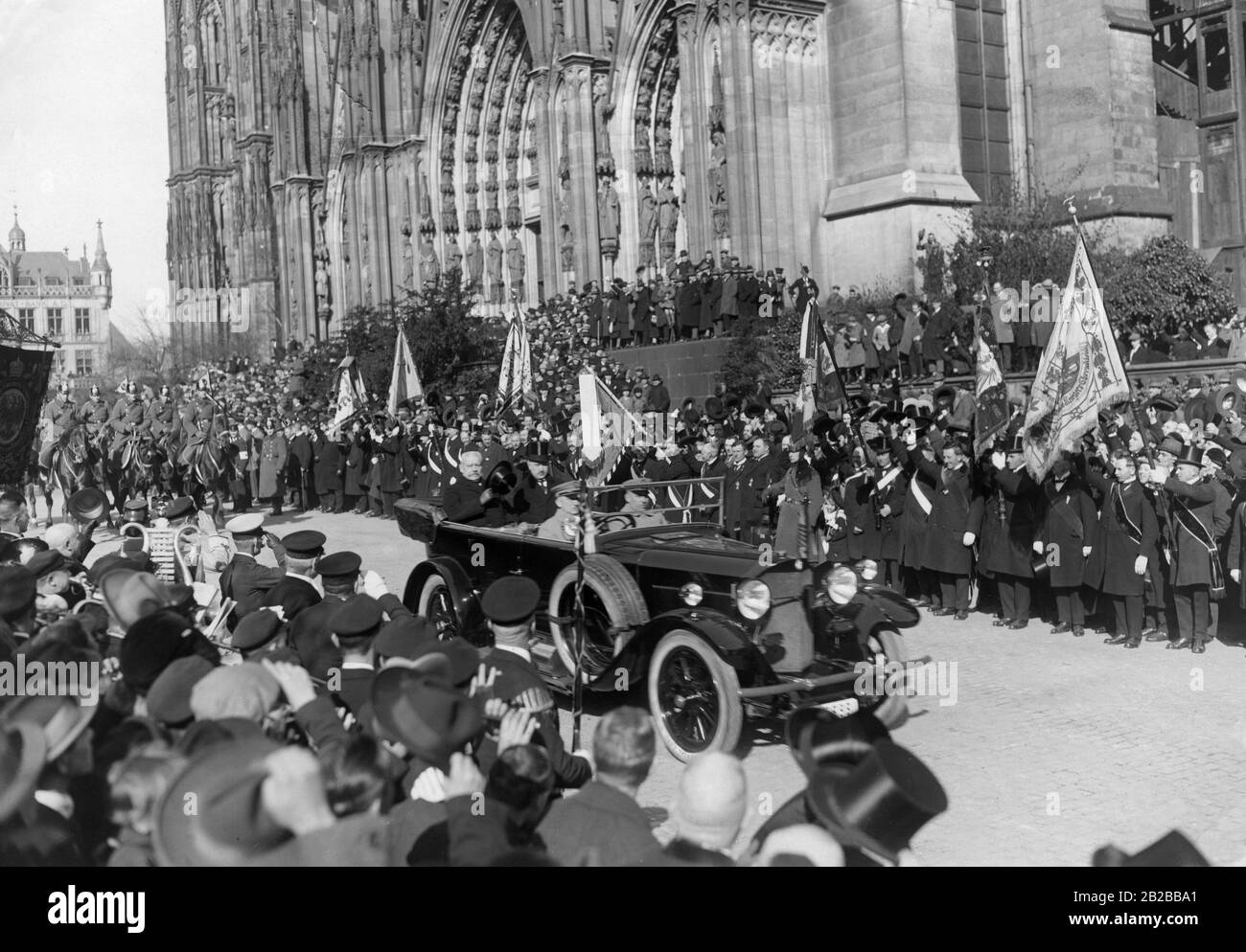 Paul von Hindenburgs (links, hinten im Auto) bei einem Besuch von Oberbürgermeister Adenauer auf dem Domplatz vor dem Kölner Dom anlässlich der "Befreiungsfeier". Auf beiden Straßenseiten stehen Zuschauer. Auf der linken Seite befindet sich eine Blaskapelle. Rechts Assoziationen mit Flaggen. Die Feier fand im Rahmen des Rückzugs der alliierten Truppen aus dem Rheinland statt. Stockfoto