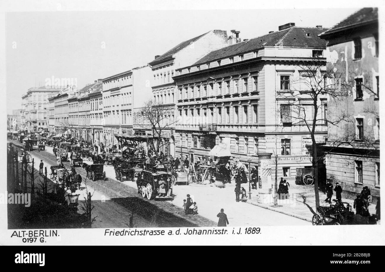 Das Bild zeigt eine alltägliche Straßenszene an der Ecke Friedrichsstraße und Johannisstraße aus dem Jahr 1889. Auf den von Geschäften umschlossenen Straßen befinden sich viele Passanten und Kutschen. Stockfoto