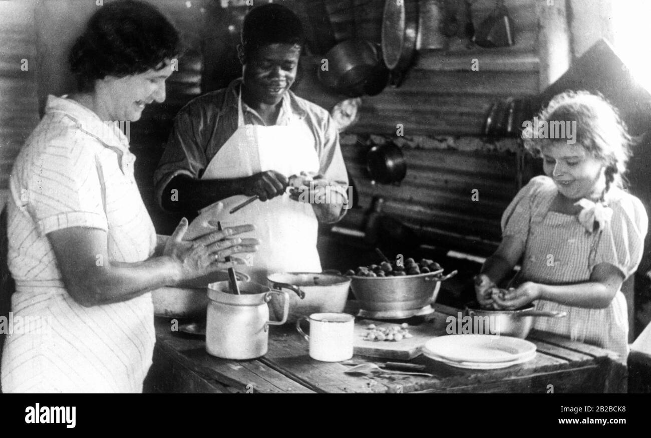 Eine deutsche Bauernfrau und ihre Tochter Inge kochen zusammen mit dem sogenannten Küchenjungen, einem Einheimischen, in der deutschen Kolonie Kamerun. Undatiertes Bild. Stockfoto