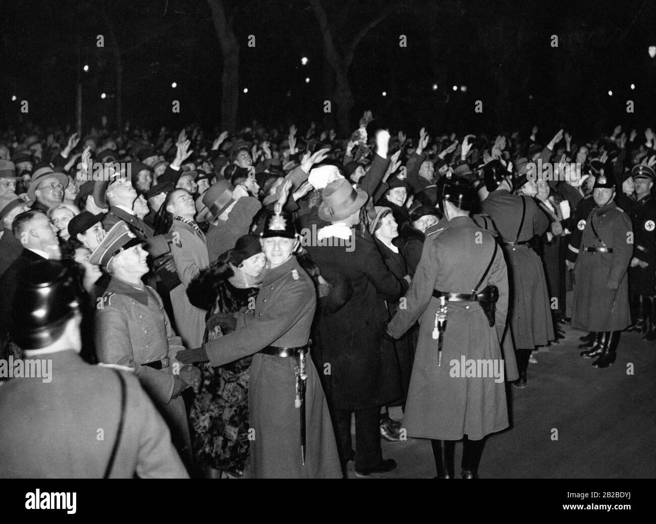 Anhänger grüßen Adolf Hitler um Mitternacht an Silvester. Viele von ihnen führen den Nazi-Salut zu seinen Ehren aus. Die Anordnung sichern Polizisten und Vertreter der Schutzstaffel SS. Stockfoto