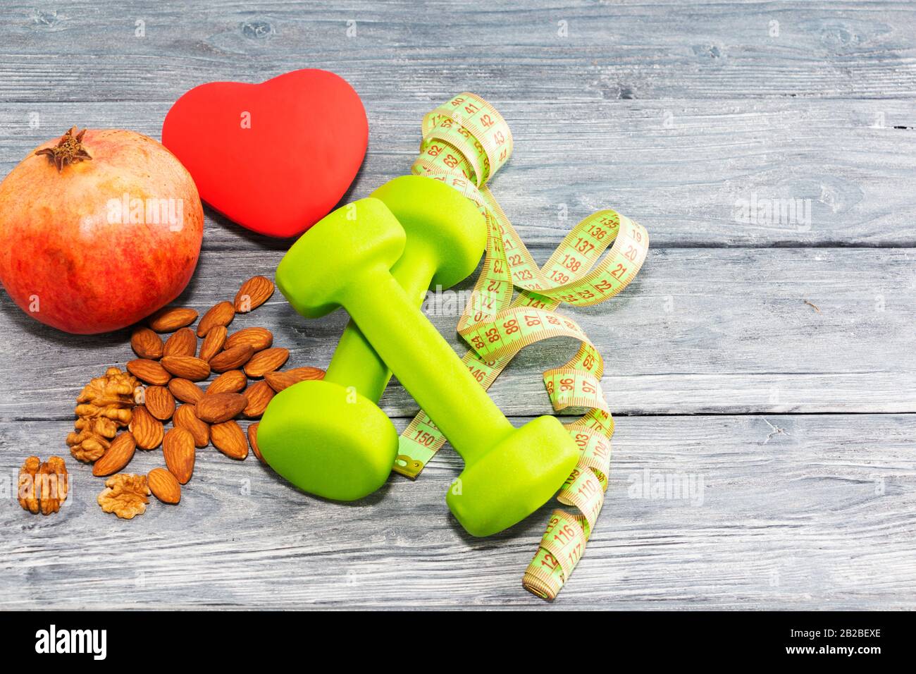 Granatapfenobst, Hanteln, Nüsse auf Holzgrund. Das Konzept der Gesundheit, des gesunden Herzens Stockfoto