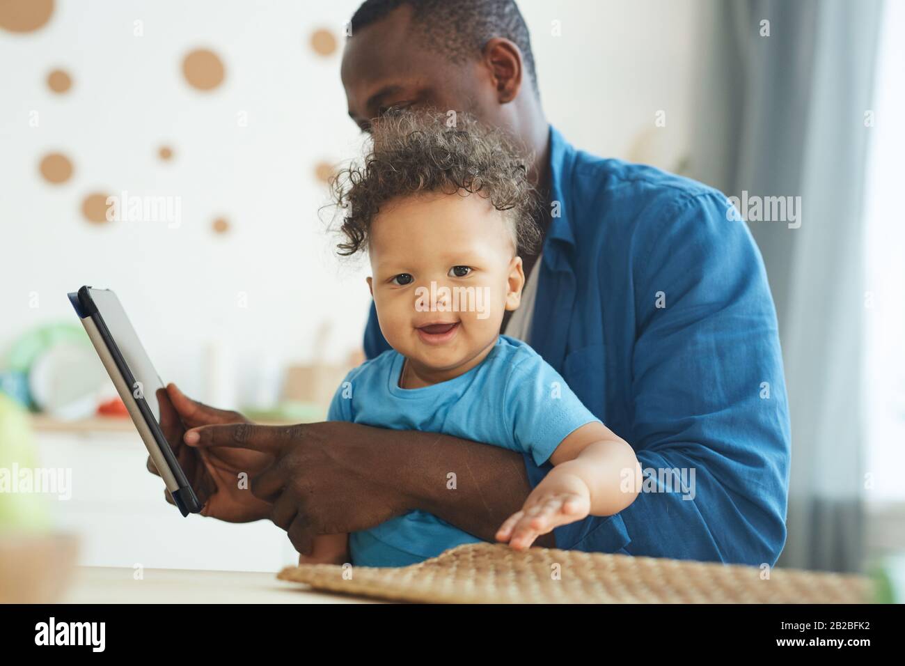 Porträt eines süßen afro-amerikanischen Kleinkindes lächelt an der Kamera, während er auf dem Schoß der Väter im Innenbereich sitzt, Kopierraum Stockfoto