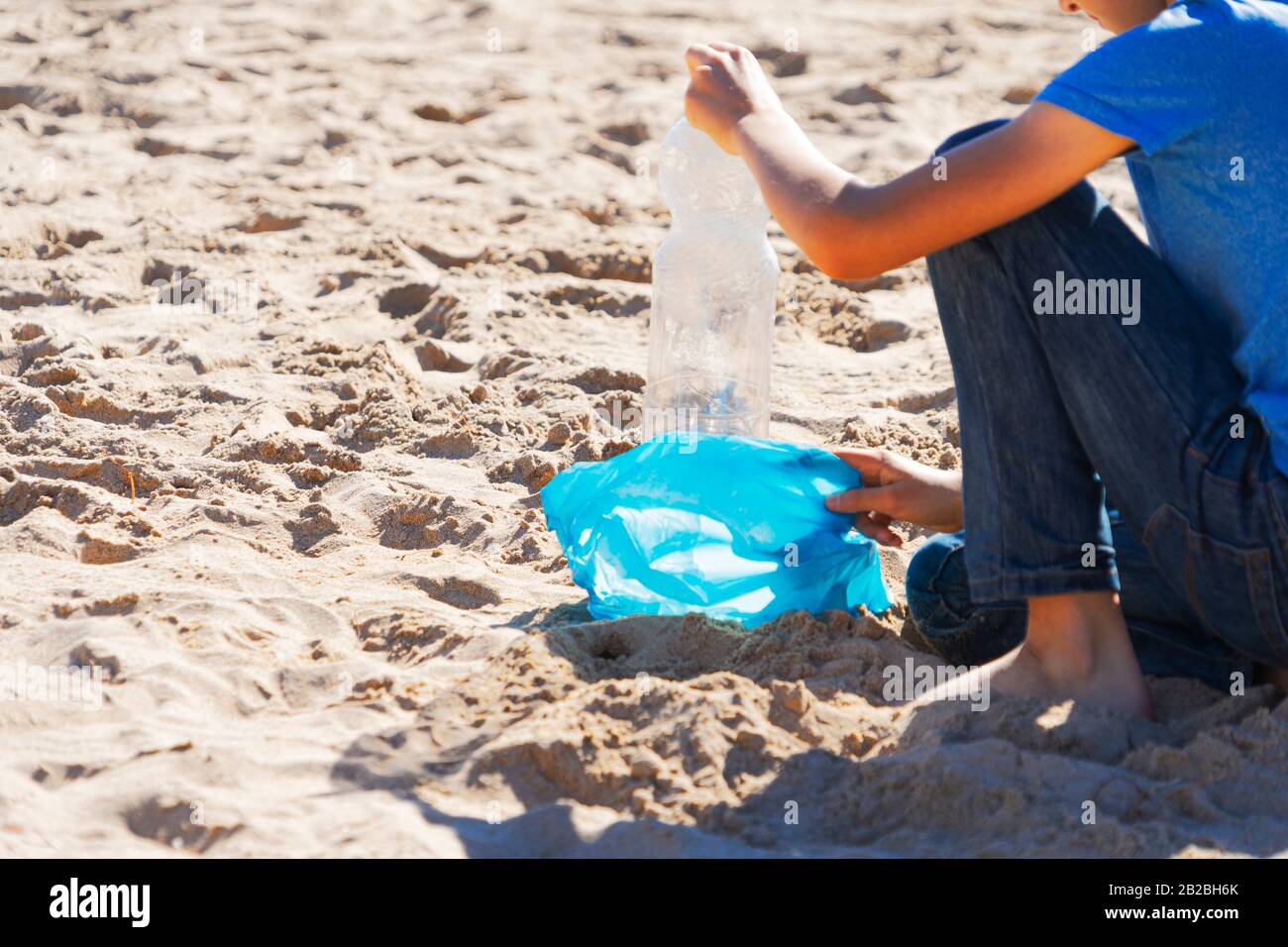 Strand aus Plastikmüll reinigen. Nehmen Sie die Plastikflasche aus dem Sand und legen Sie sie zum Recycling in einen Plastikbeutel Stockfoto