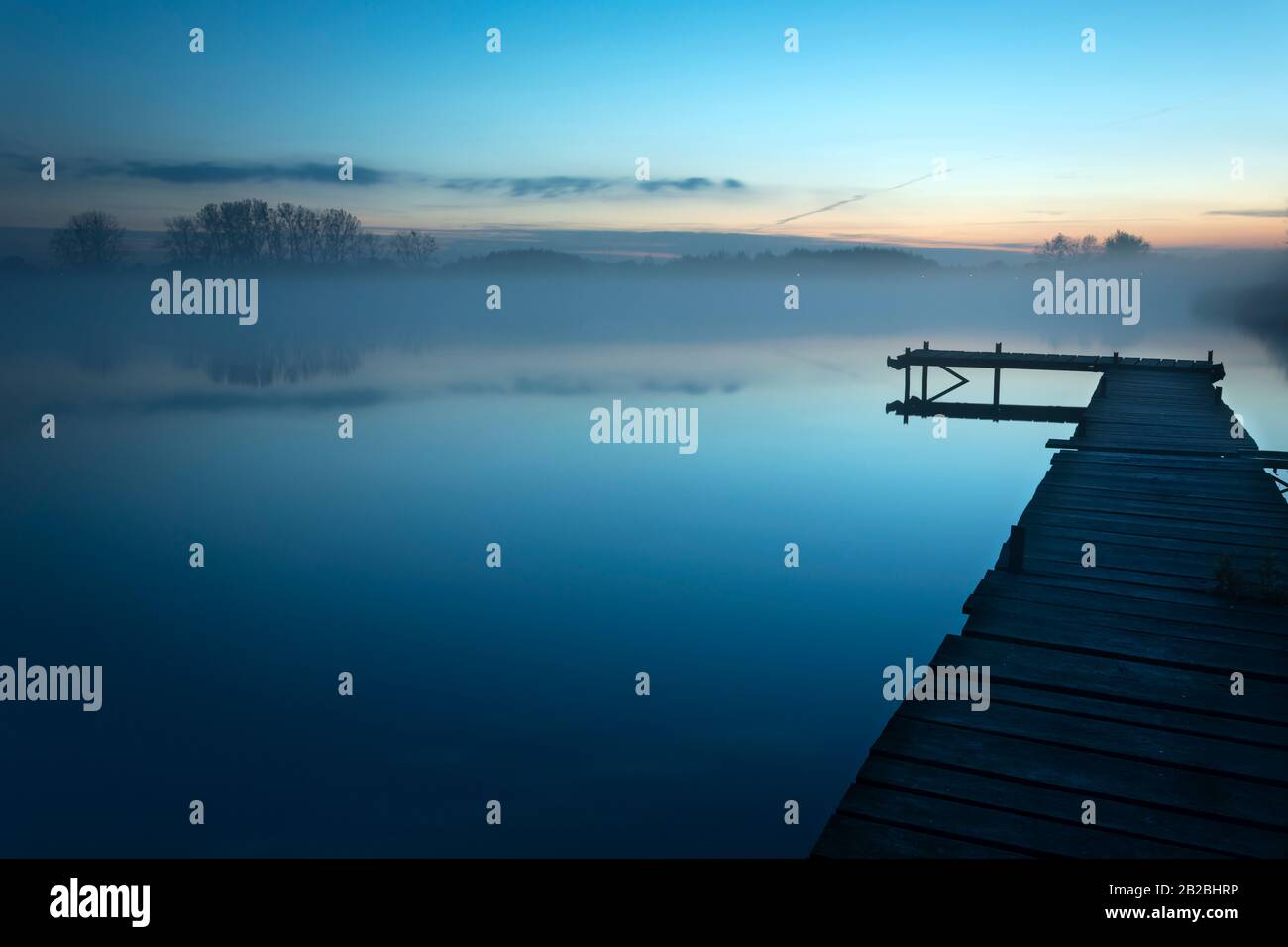 Nebeliger Abend am See mit langer Brücke Stockfoto