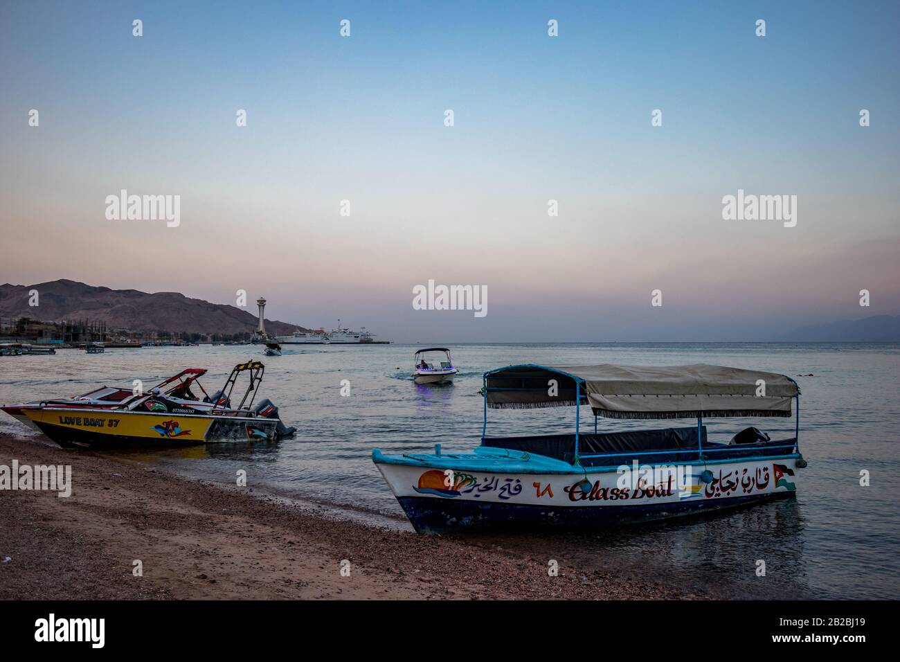 Aqaba, JORDANIEN - 31. JANUAR 2020: Sehr früh morgens warten Glasboote auf neugierige Touristen, Strand der Stadt. Winter klarer Urlaubshimmel um Sonnenaufgang. Rotes Meer, Haschemitisches Königreich Jordanien Stockfoto