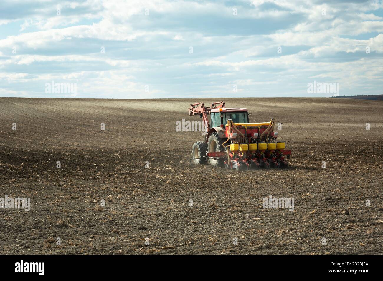 Traktor befruchtet das gepflügte Feld, Wolken und Himmel Stockfoto