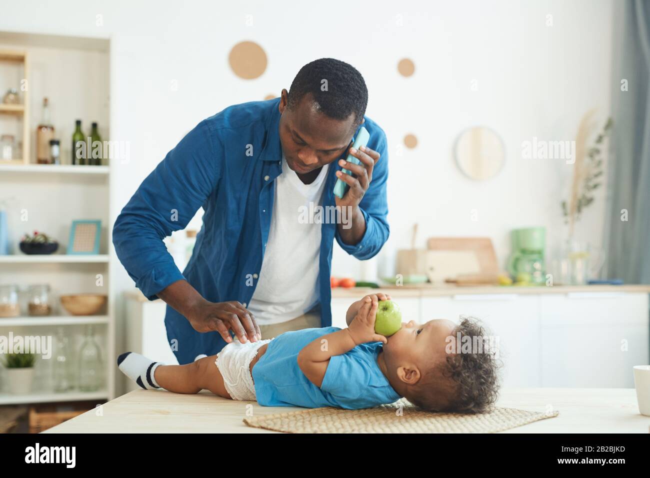 Portrait eines reifen Afrikaners, der Frau anruft, während er Windel zu Baby im Innenleben wechselt, Kopierraum Stockfoto