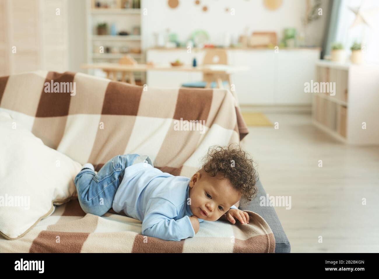 Komplettes Portrait des süßen afro-amerikanischen Babys, das auf der Couch im gemütlichen Innenbereich des Hauses liegt, Platz für Kopien Stockfoto