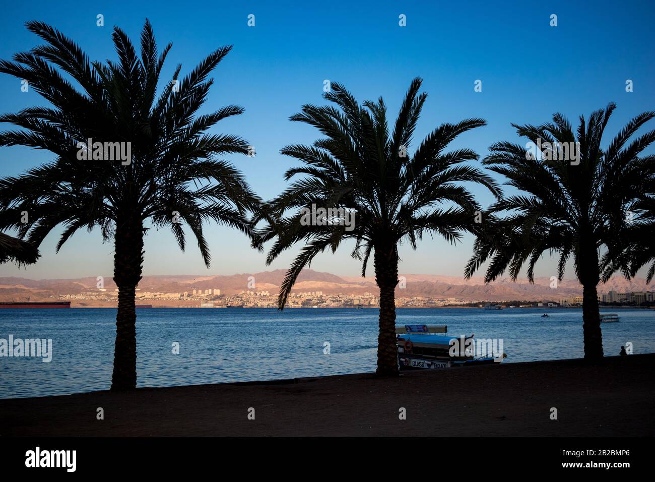Aqaba, JORDANIEN - 31. JANUAR 2020: Glasboot wartet auf Touristen, Schatten am Strand der Stadt.Palme Silhouetten.Sonnenaufgang Landschaft von Ägypten und Israel, Winter klarer Himmel.Rotmeergulf,Haschemite Königreich Jordanien Stockfoto