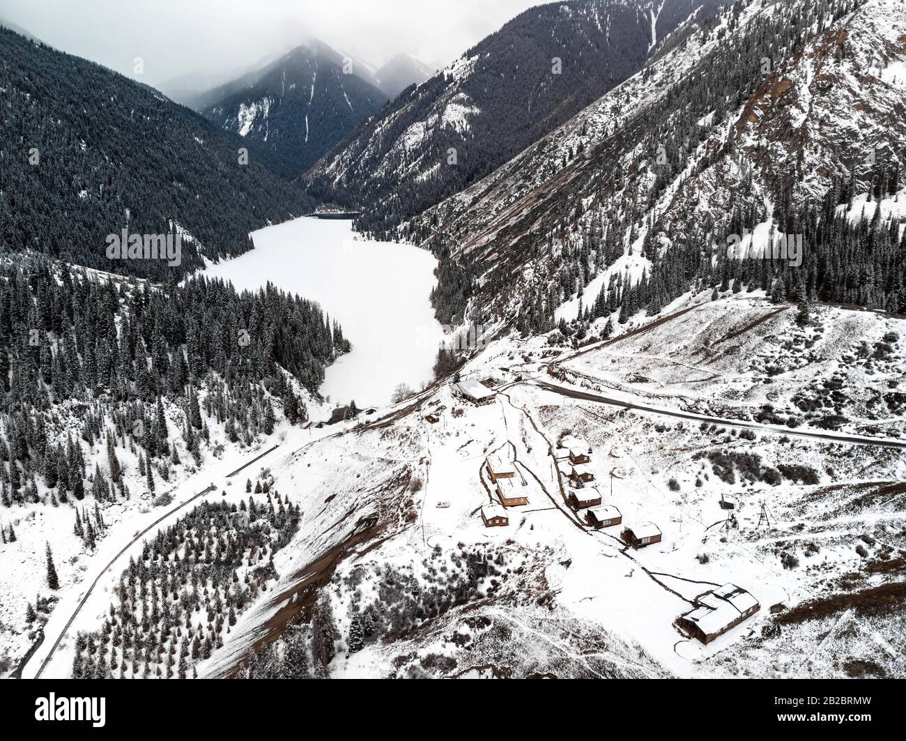 Luftbild zum Bergsee Kolsay und Dorfhäuser zur Winterzeit in den Bergen Kasachstans. Drohnenschuss, Draufsicht. Stockfoto