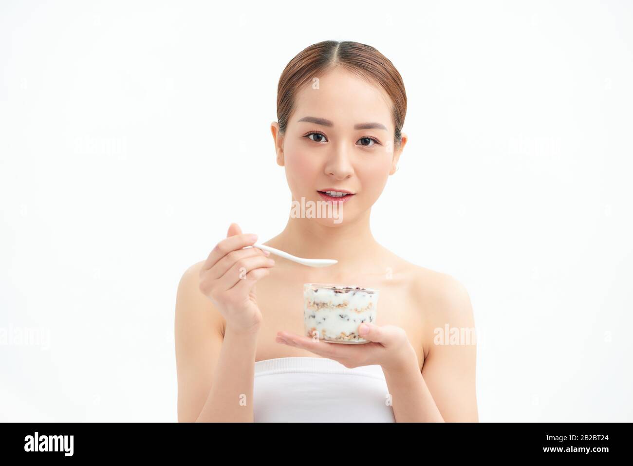 Gesunde Essende Frau. Nahaufnahme der schönen fröhlichen jungen Frau, die morgens ein Glas mit Naturjoghurt, köstlicher Rosine und Müsli hält Stockfoto