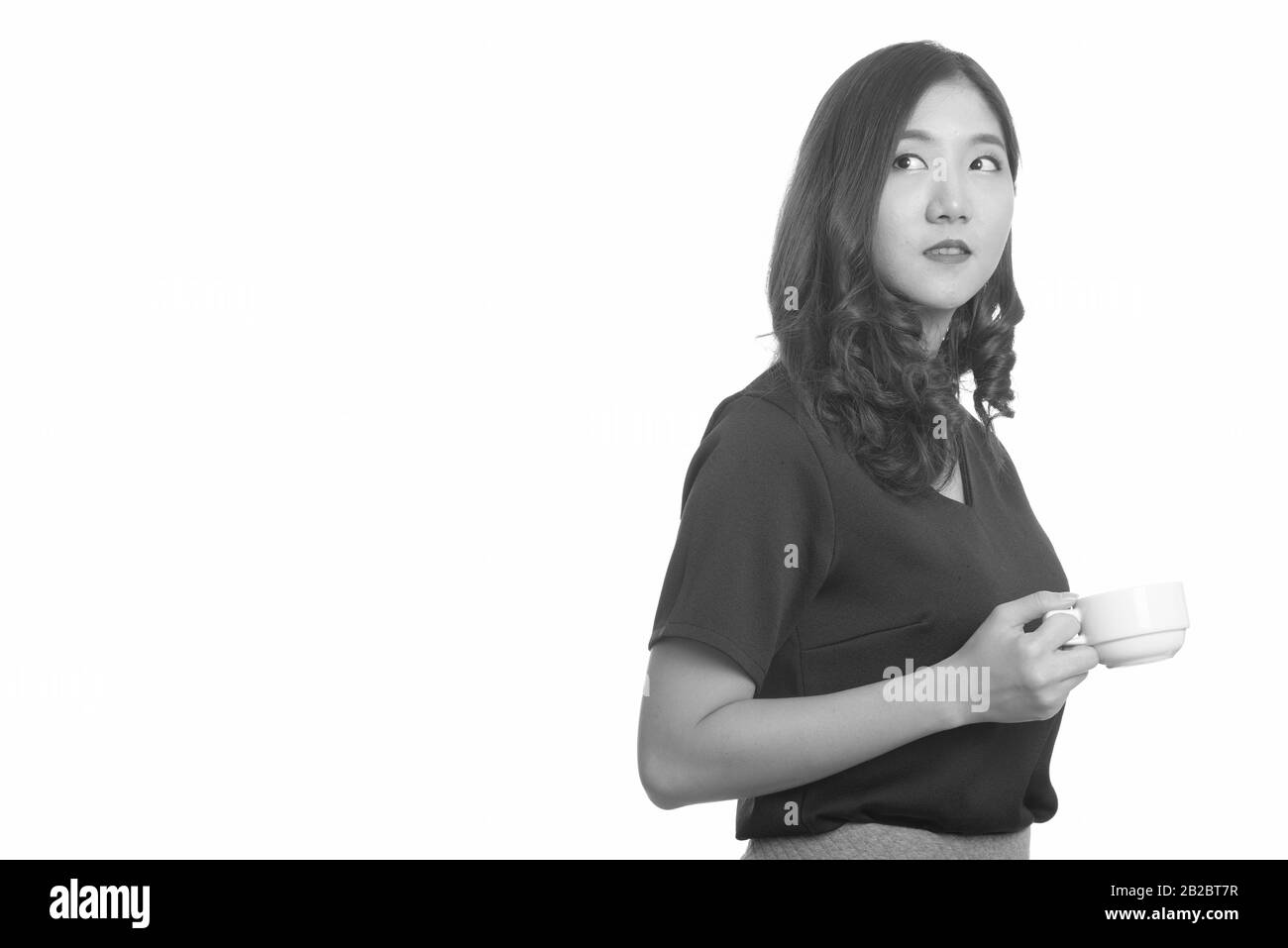 Junge, schöne asiatische Geschäftsfrau, die während des Denkens eine Tasse Kaffee hält Stockfoto