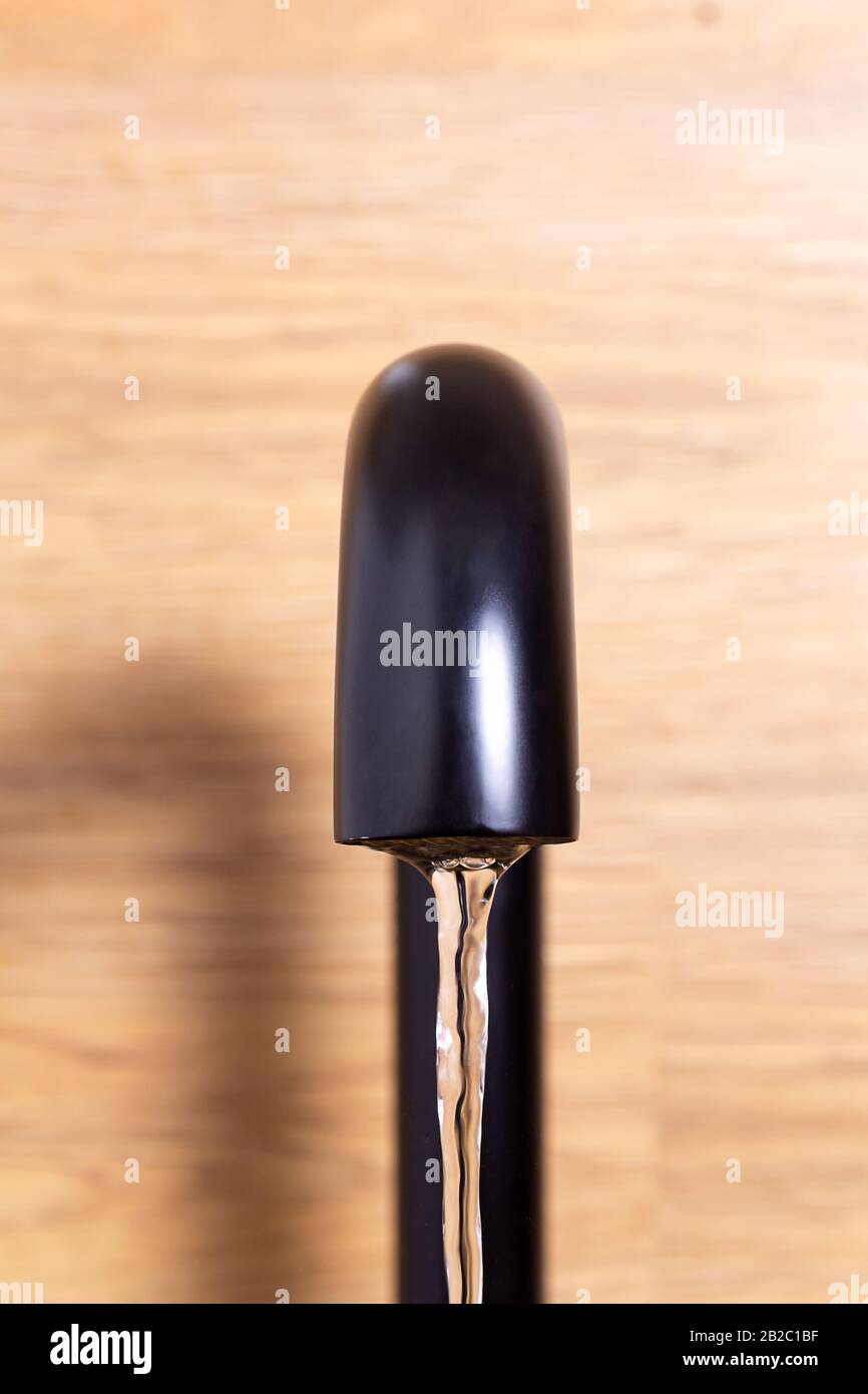 Wasserfluss aus Küche moderner schwarzer Hahn. Vertikales Foto. Wassersparkonzept. Selektiver Fokus. Küchenarmatur. Unnötige Wasserabfälle im Wor Stockfoto