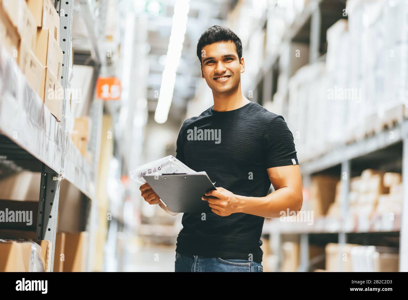 Kluger Indien-Ingenieur-Arbeiter, der die Produktverwaltung in Kartons in Regalen im Lager vorräte. Inventuranzahl des Werks. Stockfoto