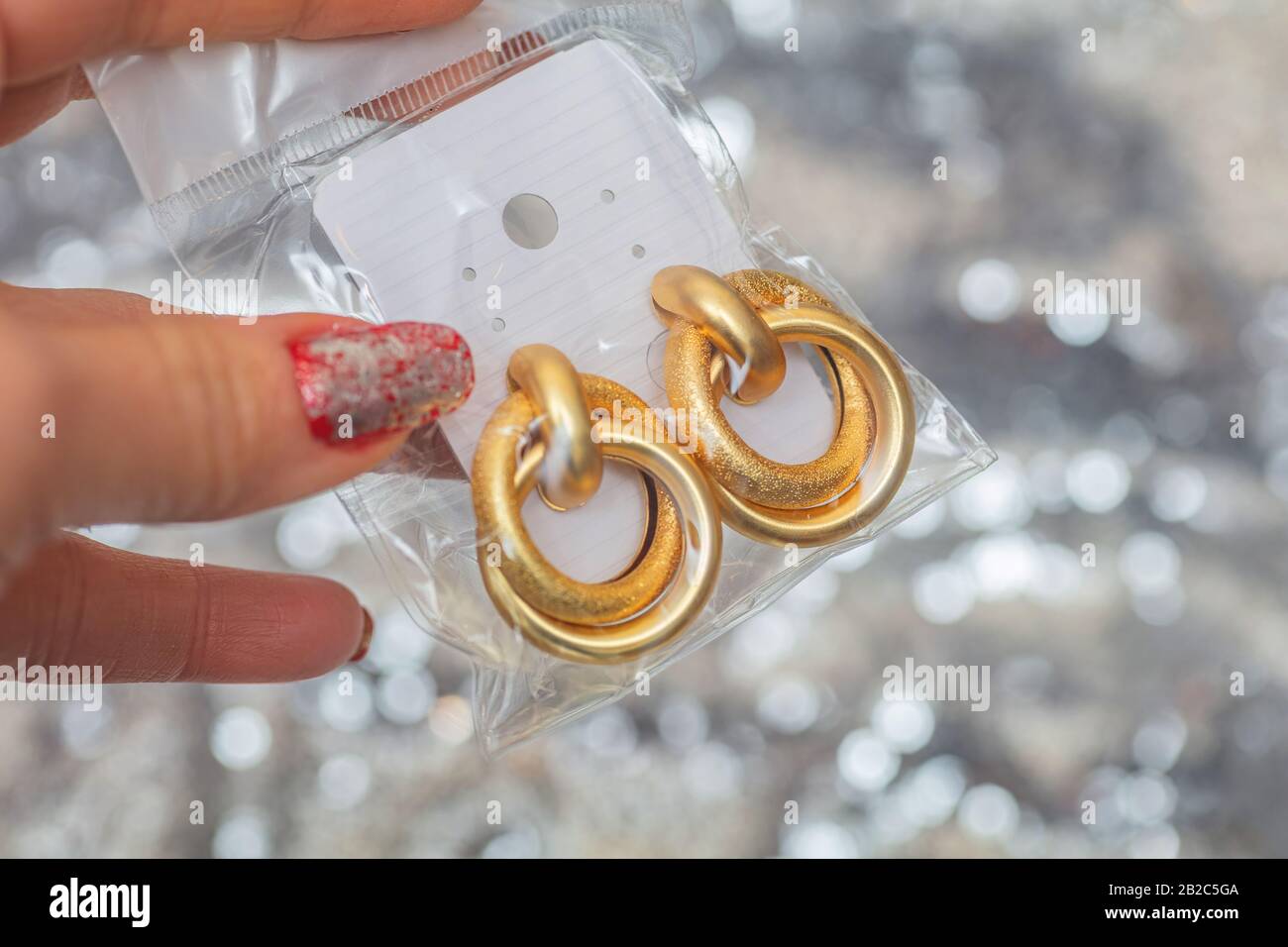 Moderne asymmetrische goldene Ohrringe mit geschichteten Ringen auf silberglänzendem Hintergrund Stockfoto