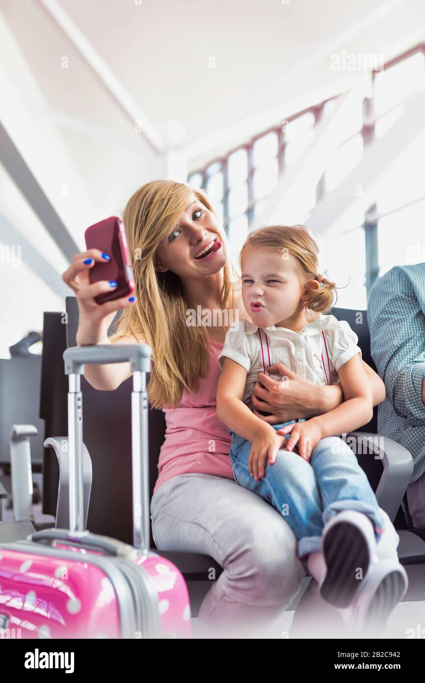 Porträt des jungen Teenager-Mädchens, das selfie mit ihrer kleinen Schwester nimmt, während sie auf das Einsteigen in den Flughafen wartet Stockfoto