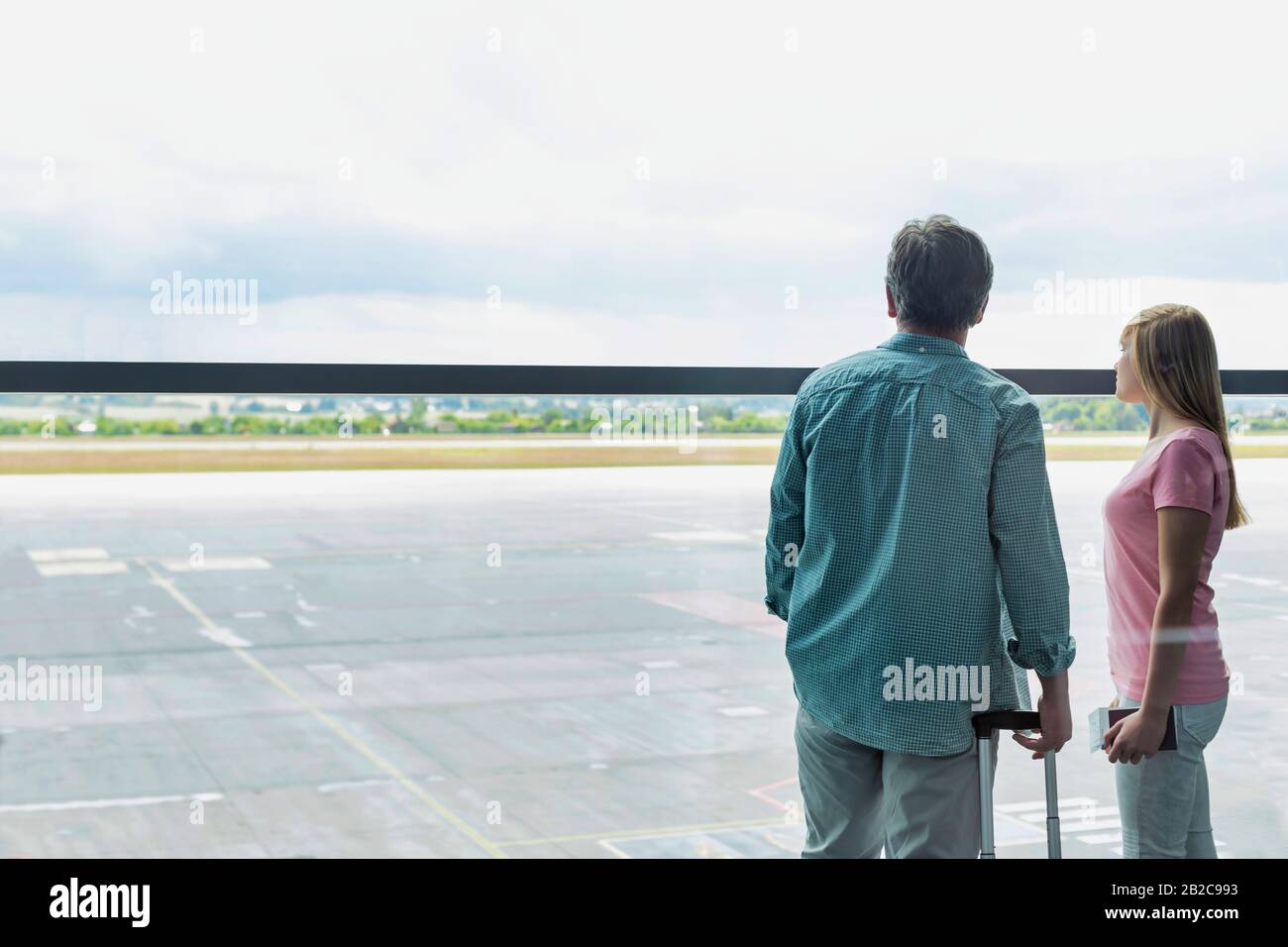 Rückansicht eines reifen Mannes, der mit seiner Tochter auf dem Flughafen durch das Fenster blickt Stockfoto