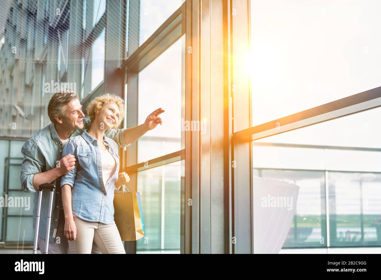 Reifer Mann umarmt seine Frau von hinten beim Blick durch das Fenster im Flughafen Stockfoto