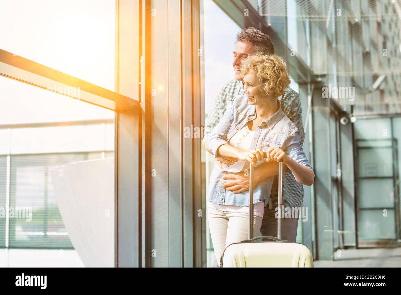 Reifer Mann umarmt seine Frau von hinten beim Blick durch das Fenster im Flughafen Stockfoto