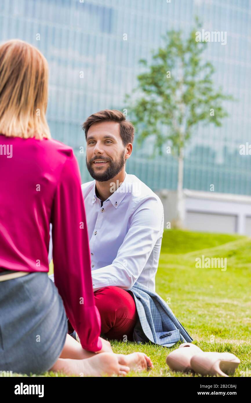 Geschäftsleute diskutieren Pläne, während sie im Freien auf dem Gras sitzen Stockfoto