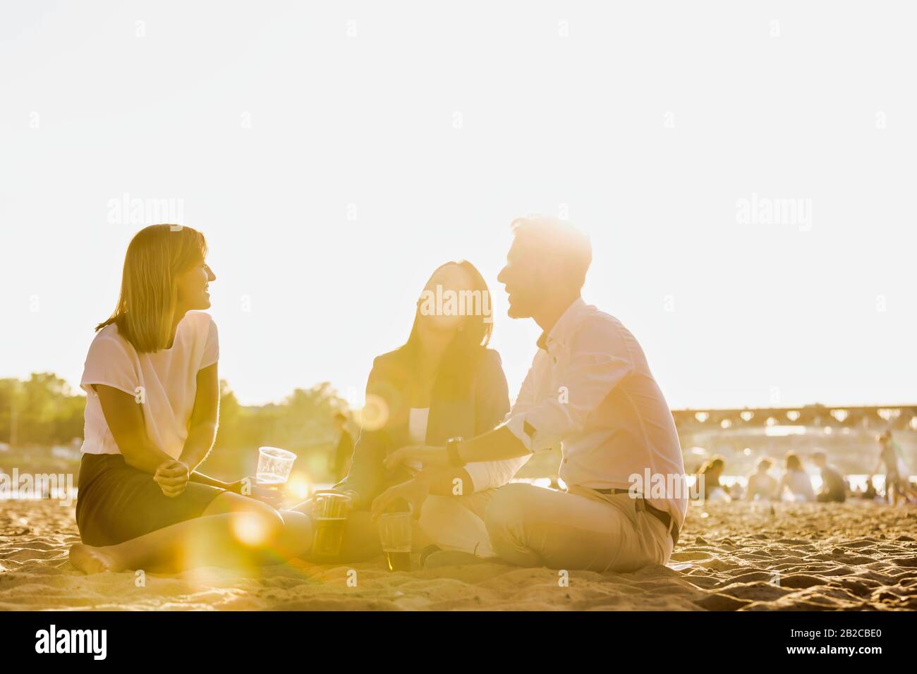 Geschäftsleute feiern Erfolg, während sie Bier am Strand mit Linsenflauge im Hintergrund trinken Stockfoto