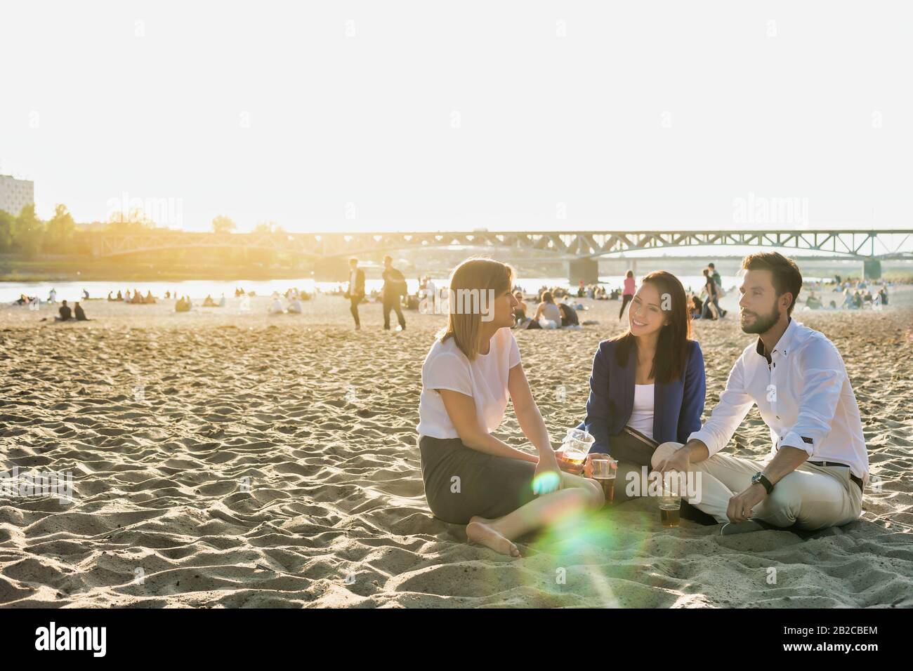 Geschäftsleute feiern Erfolg, während sie Bier am Strand mit Linsenflauge im Hintergrund trinken Stockfoto