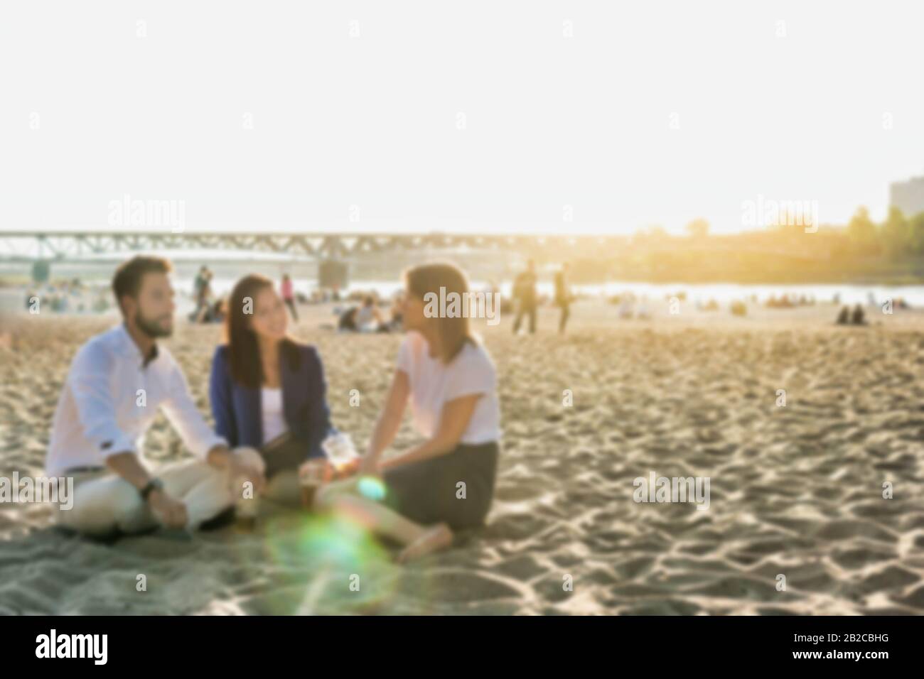 Geschäftsleute feiern Erfolg, während sie Bier am Strand mit Linsenflauge im Hintergrund trinken Stockfoto