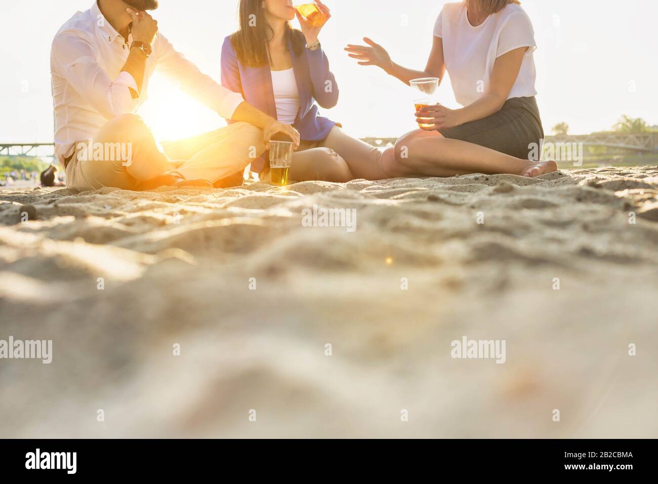 Geschäftsleute feiern Erfolg, während sie Bier am Strand mit Linsenflauge im Hintergrund trinken Stockfoto
